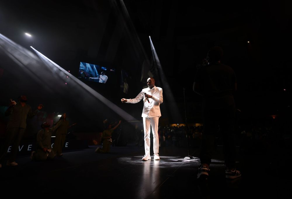 Solo performer in white suit illuminated by spotlight on dark concert stage.