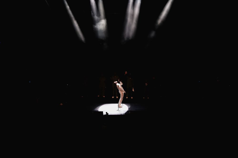 Dramatic spotlight illuminates solo performer on dark stage.