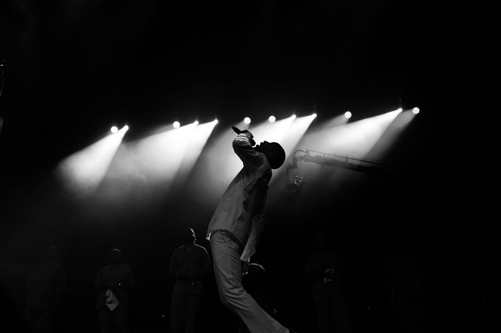 Black and white silhouette of performer in dramatic pose under stage spotlights.