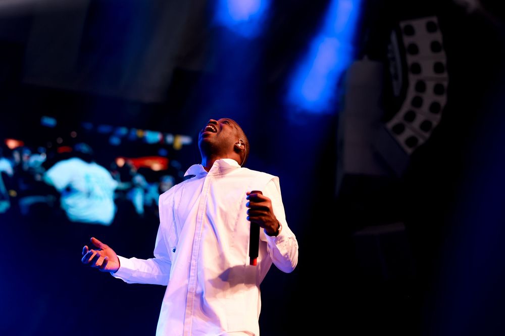 Performer in white outfit singing passionately against blue-lit stage background.