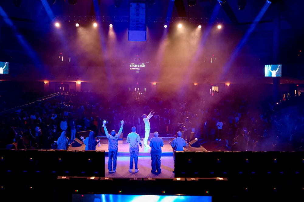 Group performance on stage with dramatic blue lighting and fog effects.