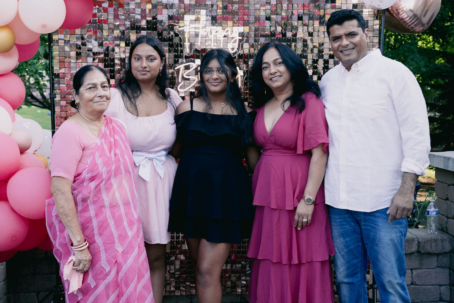 A group poses together at a celebration decorated with pink balloons and floral backdrop.