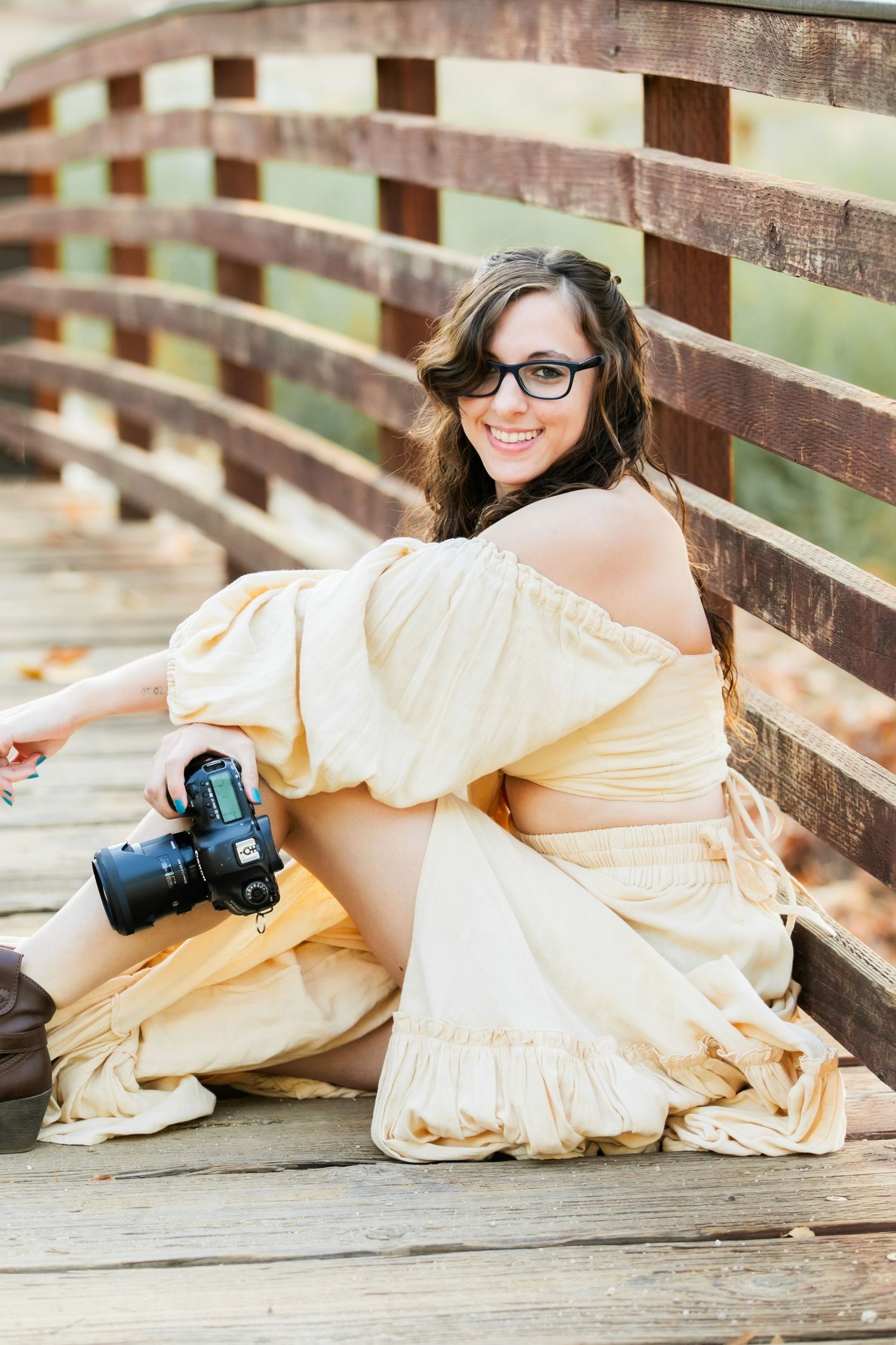 photographer Ashley Ann Imagery sitting on a bridge while holding a camera in one of her hands