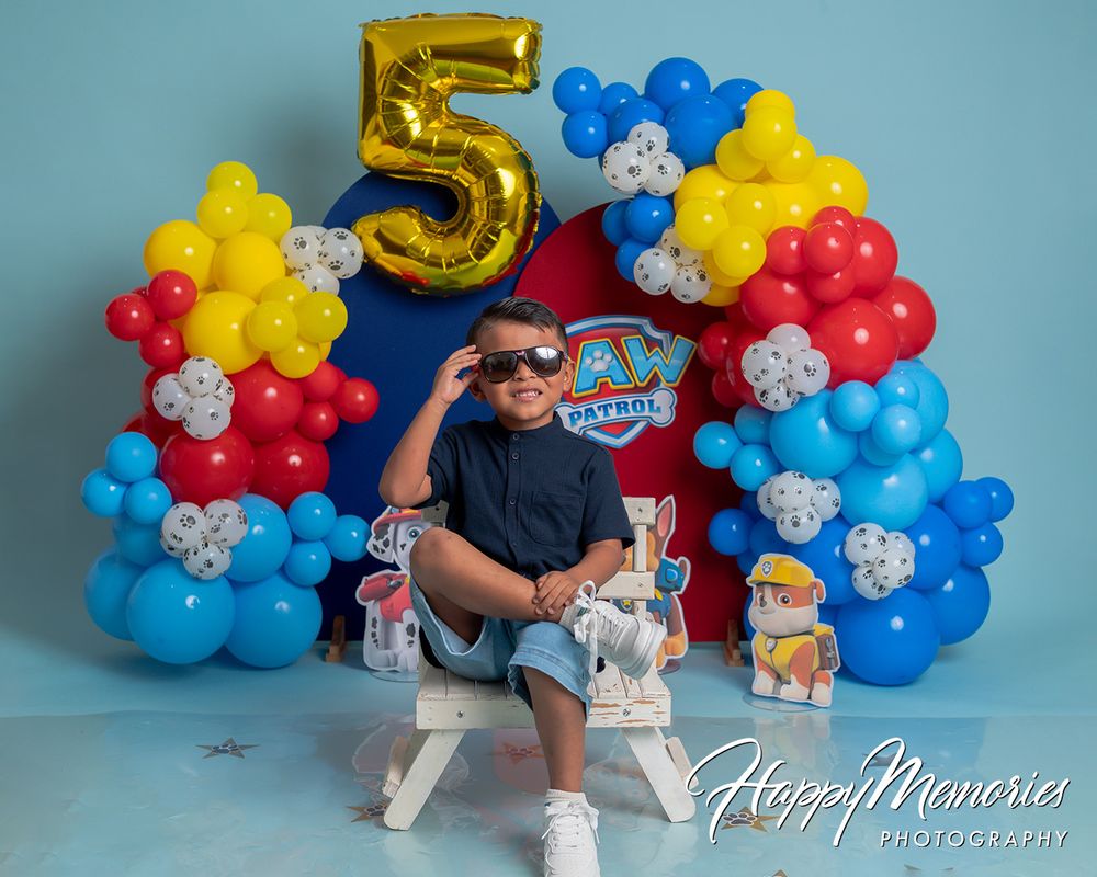 Boy celebrates 5th birthday with PAW Patrol balloon arch in red, blue, and yellow at a Happy Memories Photography session.