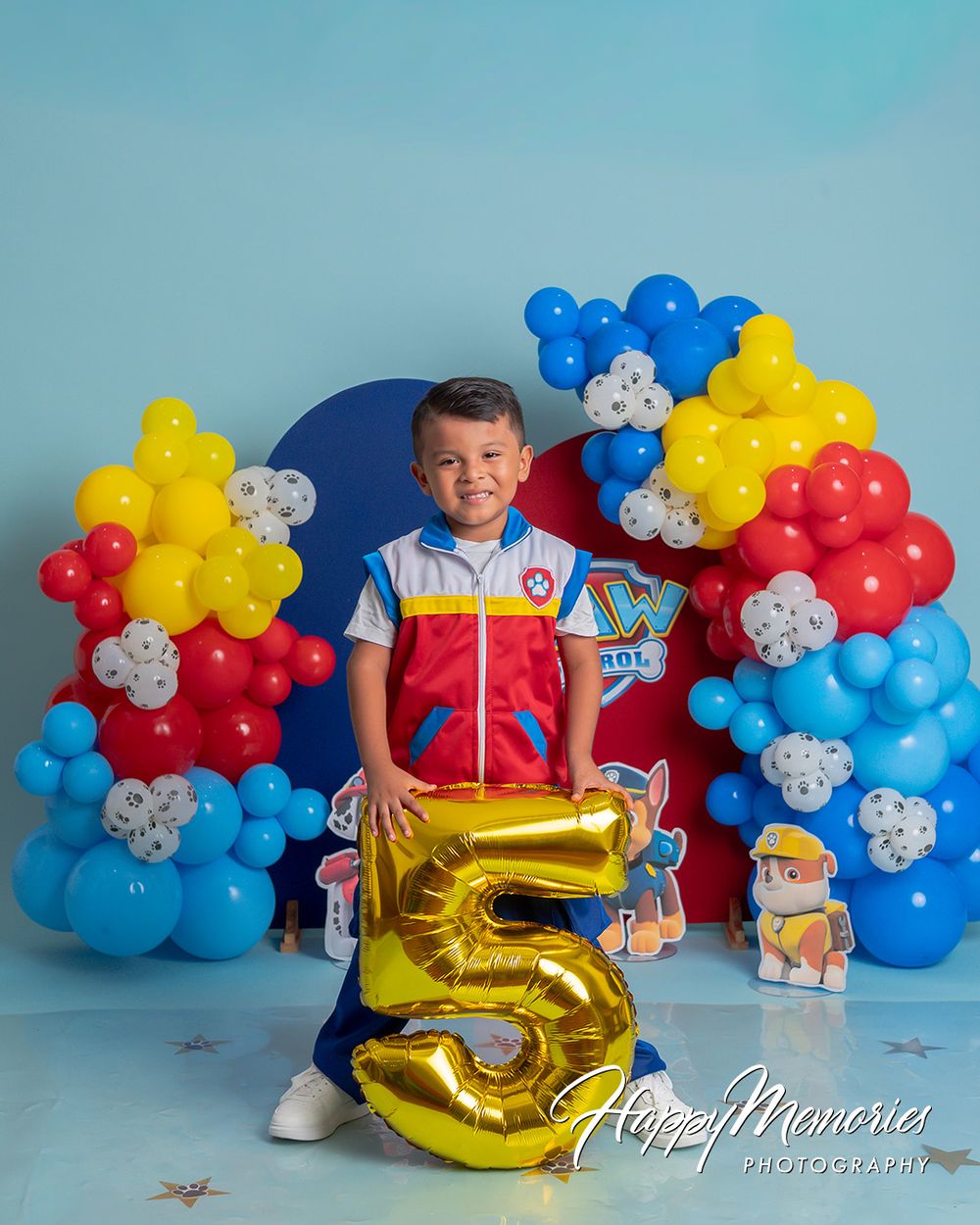 Boy holding gold number 5 balloon at Paw Patrol birthday party with colorful balloon arch backdrop.