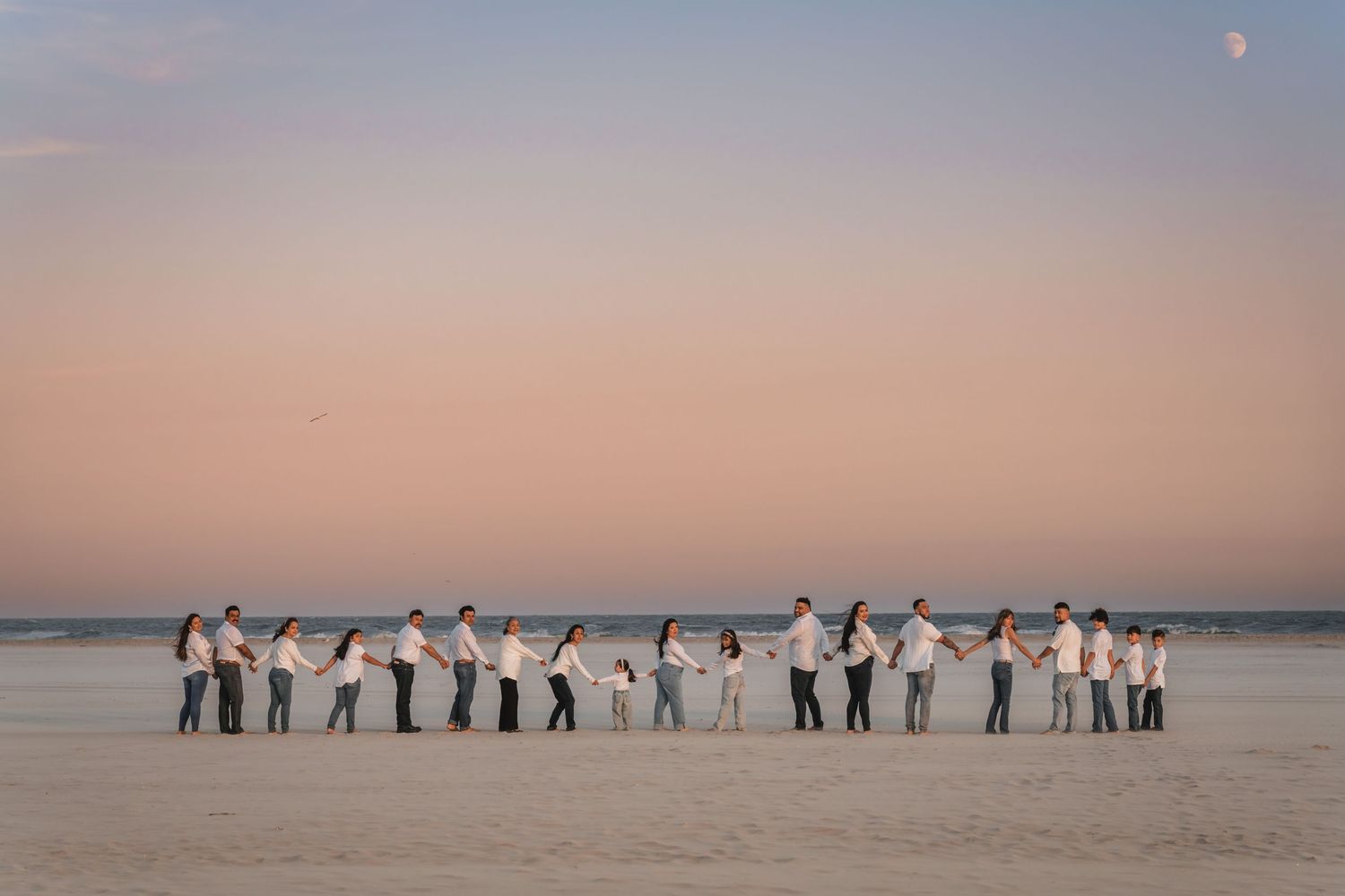 Large extended family holding hands in a long line on the beach at sunset.
