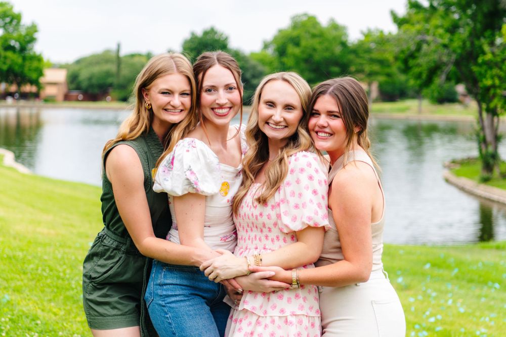 Friends pose together for photos outdoors near a waterfront.
