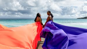 Colorful fabric flowing in the wind against a tropical beach and ocean backdrop.