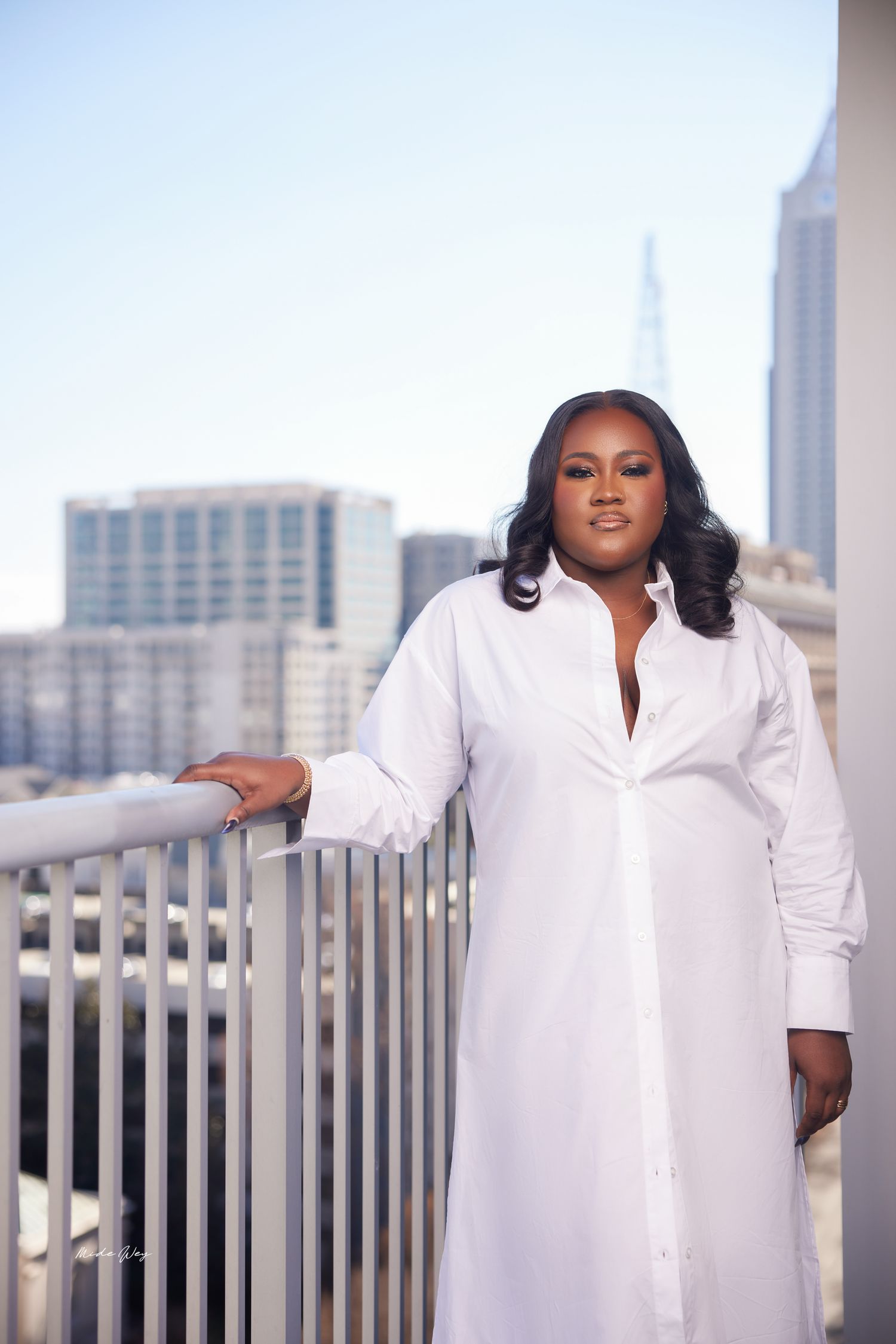 Woman in white dress poses confidently on urban rooftop with city skyline in background.