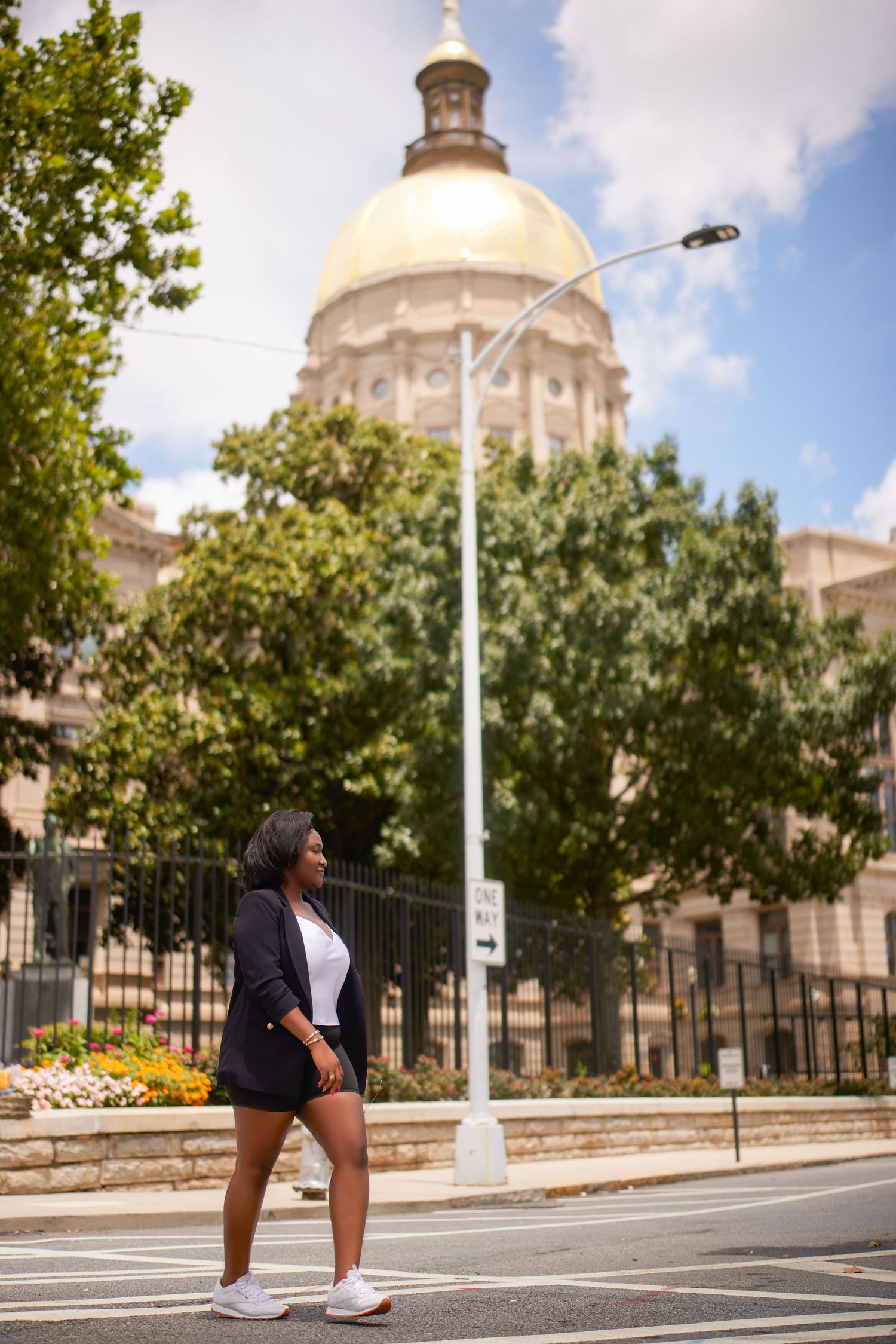 Athletic person stretches and exercises on a city street near a domed building with trees and flowers in background.