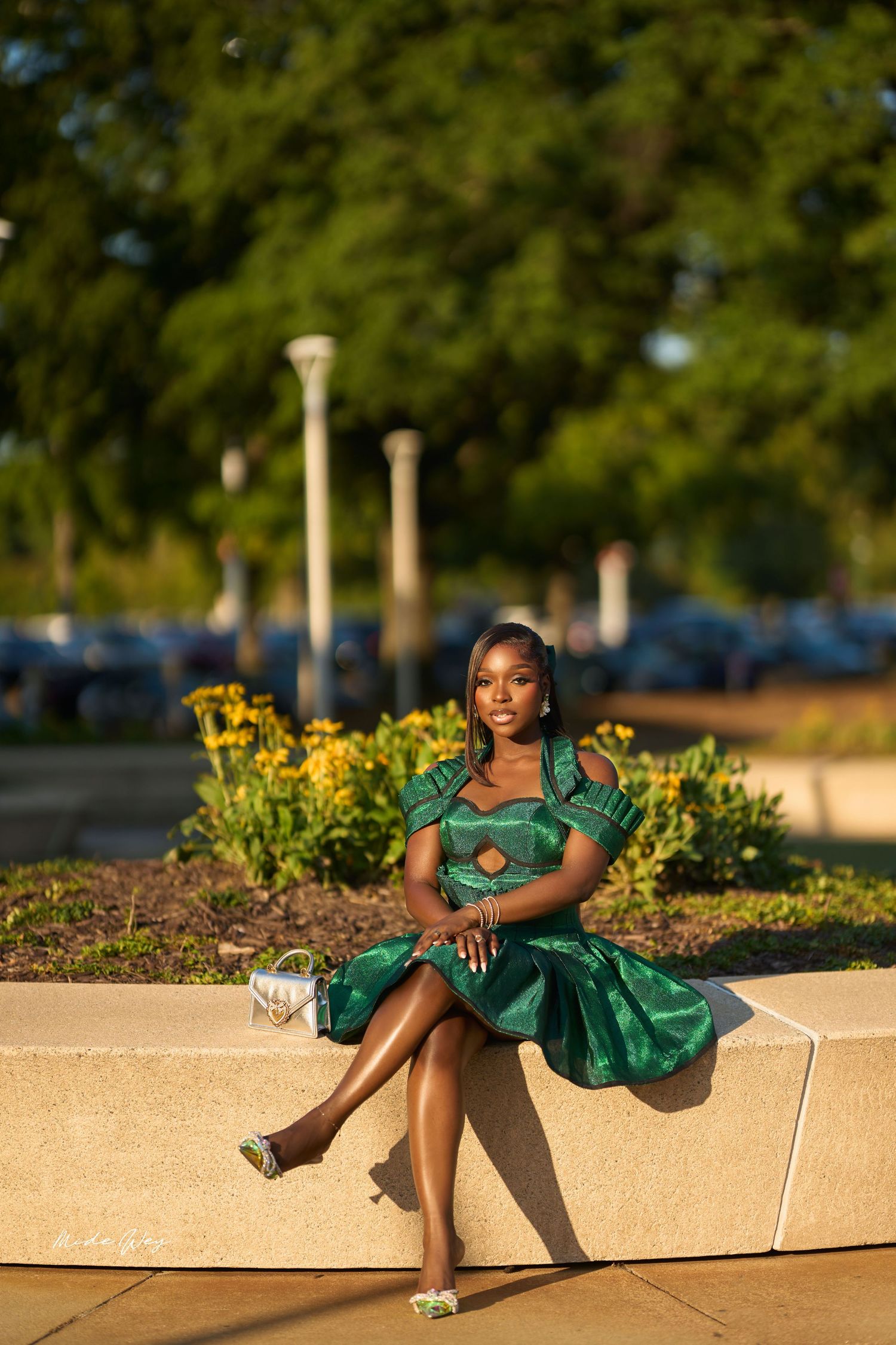 A person in an emerald green dress poses gracefully on a concrete ledge during golden hour.