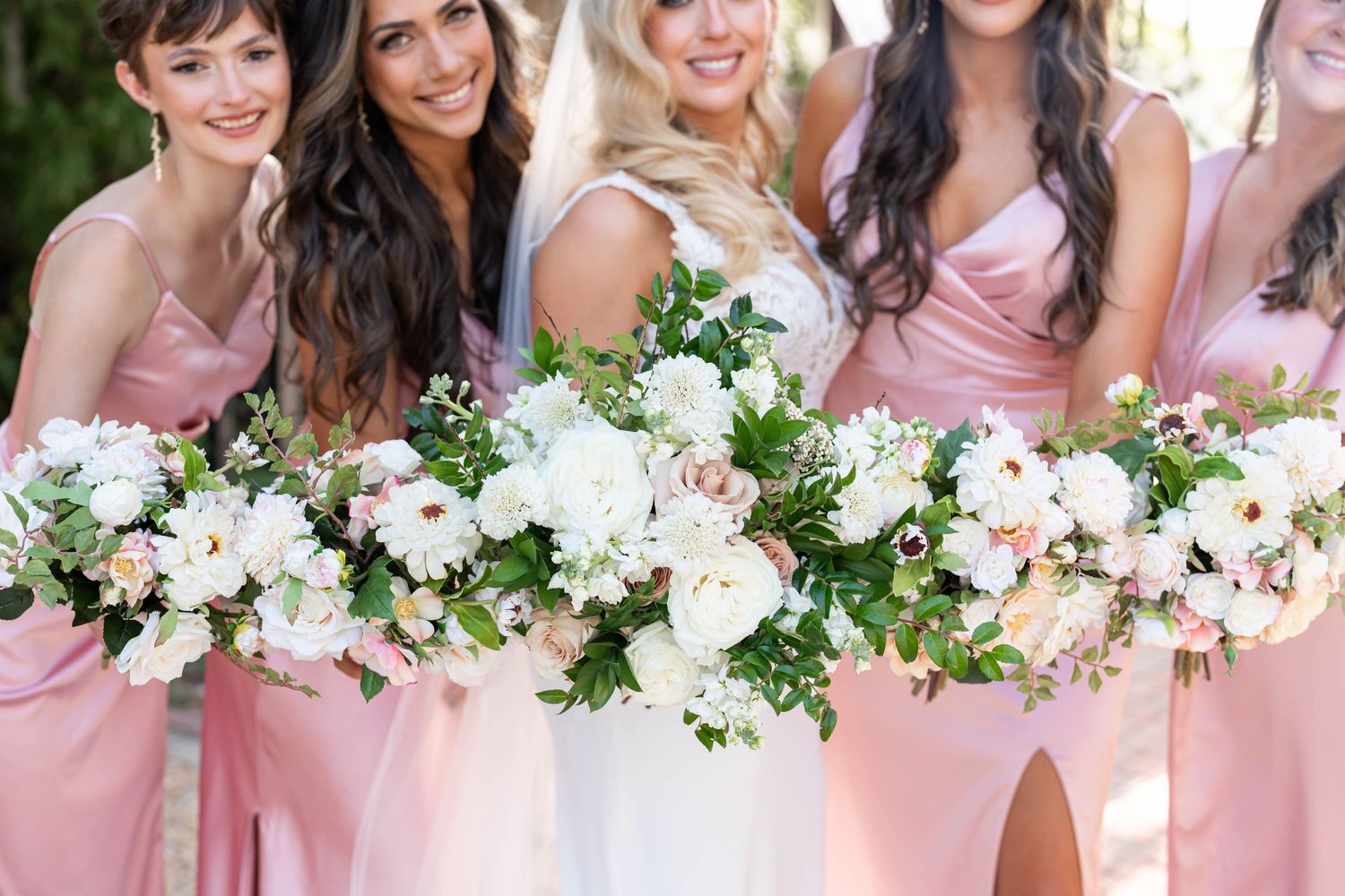 Bridesmaids in pink dresses holding elegant white and blush floral bouquets.