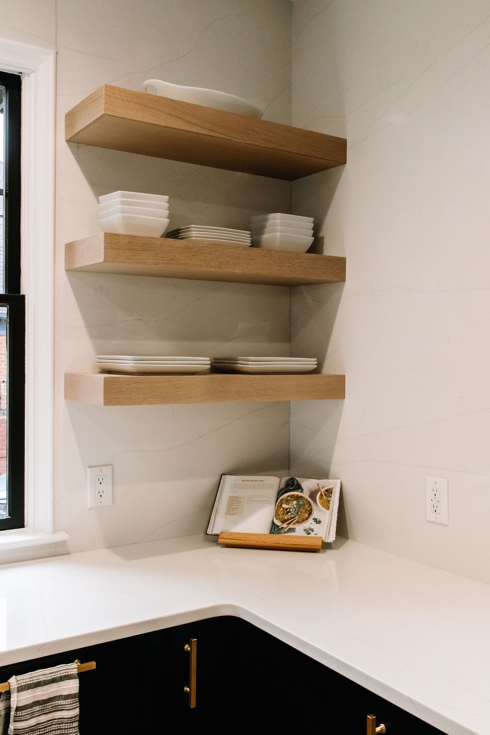 Floating wood shelves with white dishware above black cabinets and quartz countertop.