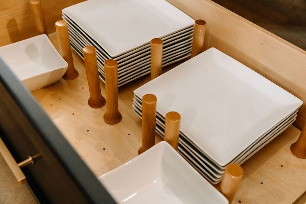 Organized kitchen drawer with white square plates and bowls neatly stacked on wooden plate holders.