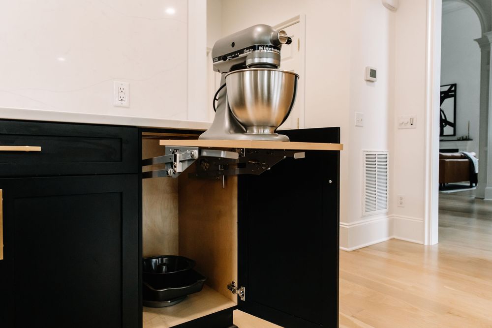Pull-out cabinet shelf revealing a stainless steel stand mixer stored inside black kitchen cabinetry.