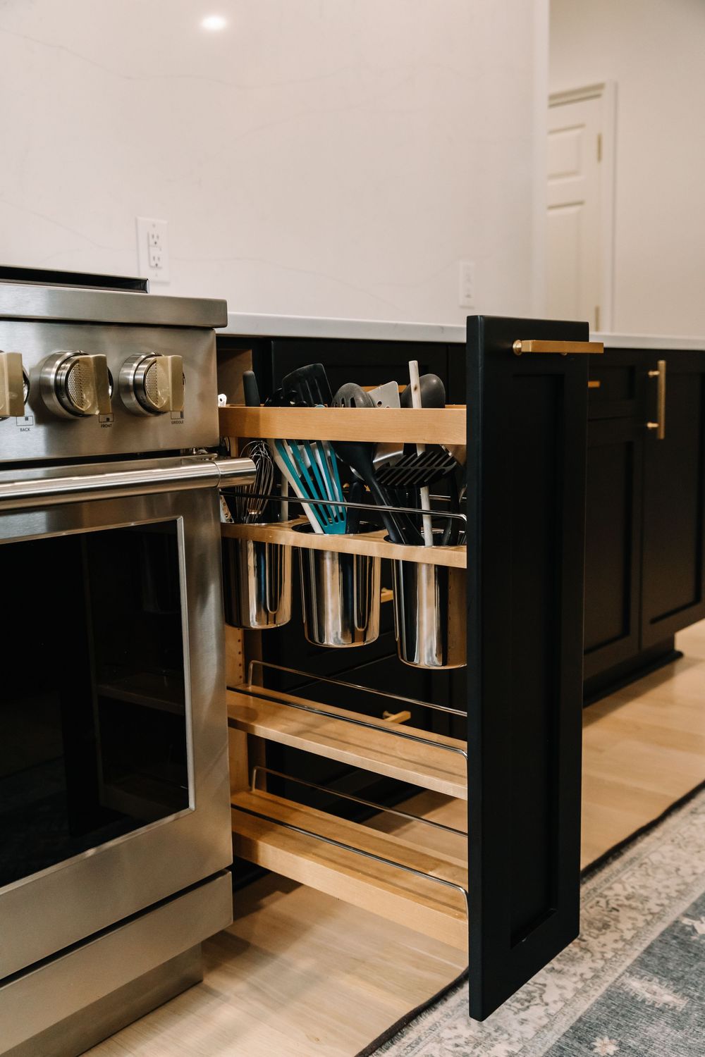 Pull-out kitchen organizer beside stainless steel range holding utensils in wooden and metal containers.