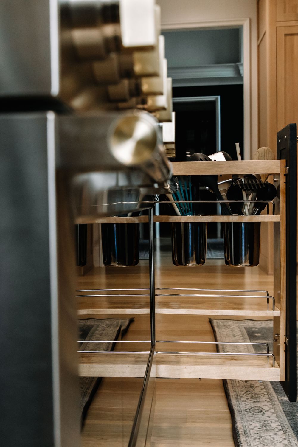 Close-up of pull-out wooden kitchen organizer with metal containers holding cooking utensils.