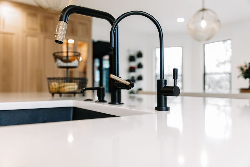 Matte black gooseneck faucet and soap dispenser on white quartz kitchen island countertop.