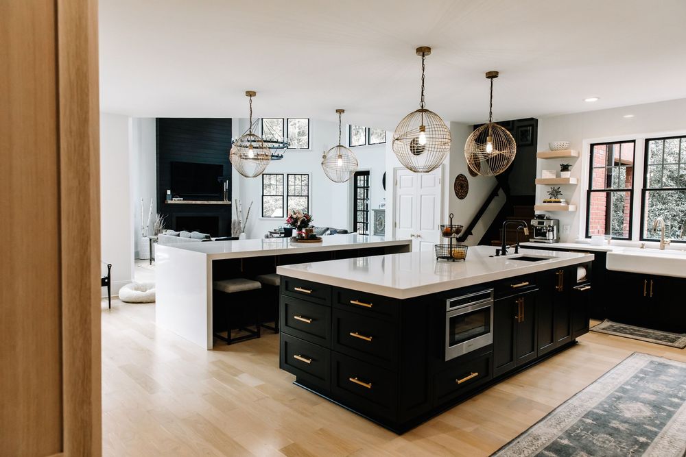 Spacious kitchen with black cabinetry, gold hardware, globe pendant lights, and light hardwood floors.