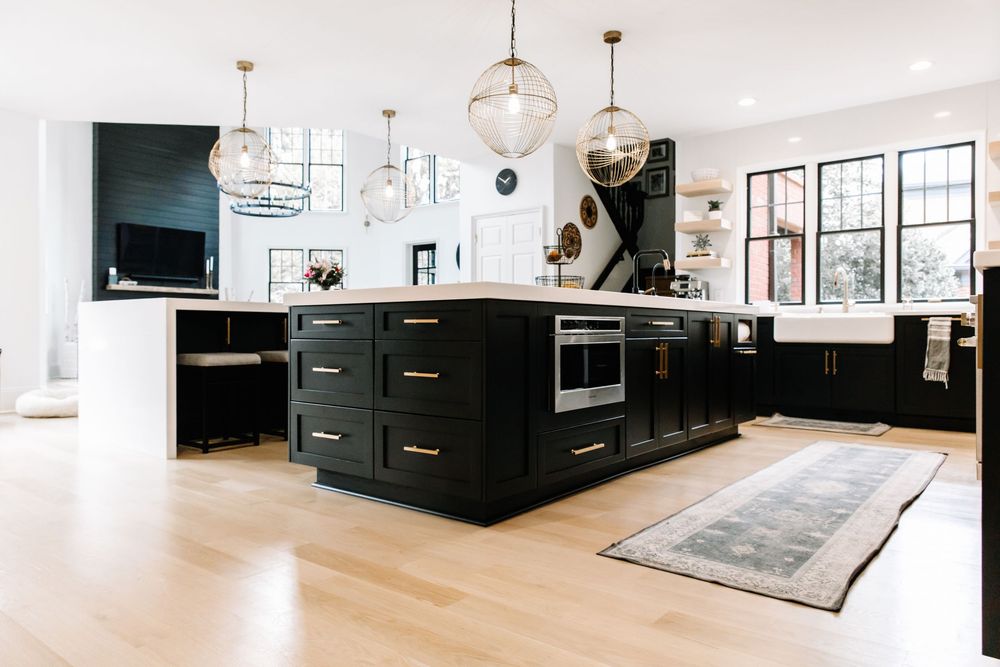 Modern kitchen featuring black island with gold pulls, globe pendant lights, and bright natural light.