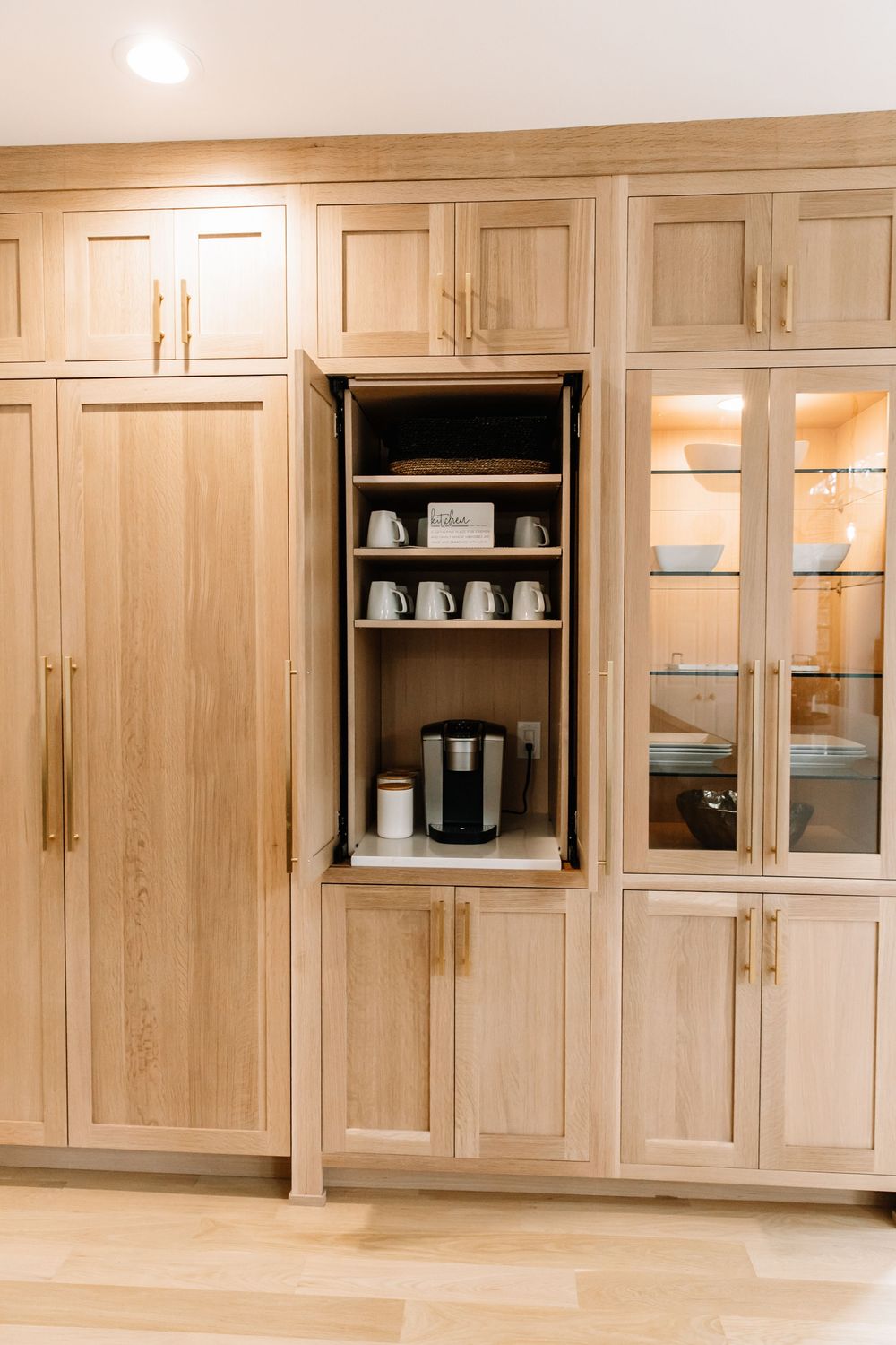 Light wood built-in cabinetry with open coffee station revealing mugs, coffee maker, and supplies.