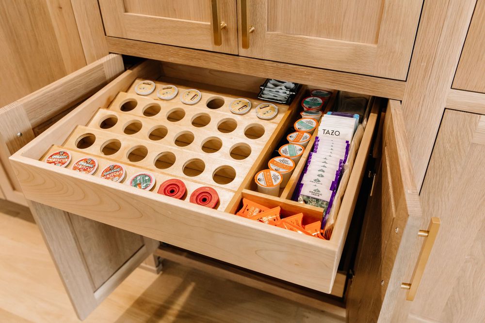 Custom wooden drawer organizer with circular cutouts storing coffee pods and tea bags in cabinetry.