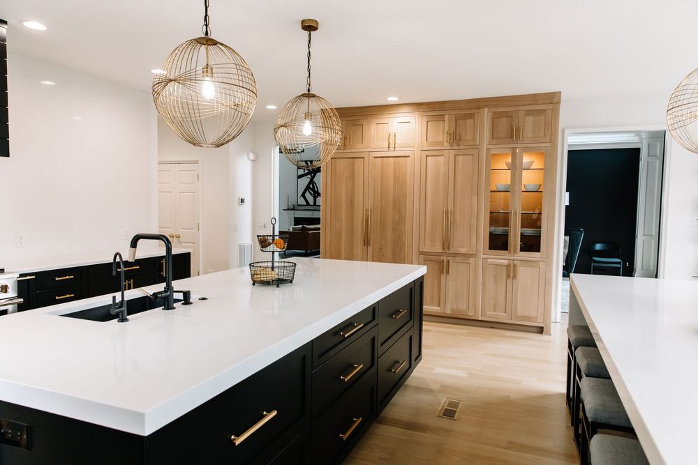 Modern kitchen with black island, white quartz countertops, gold pendant lights, and natural wood cabinetry.