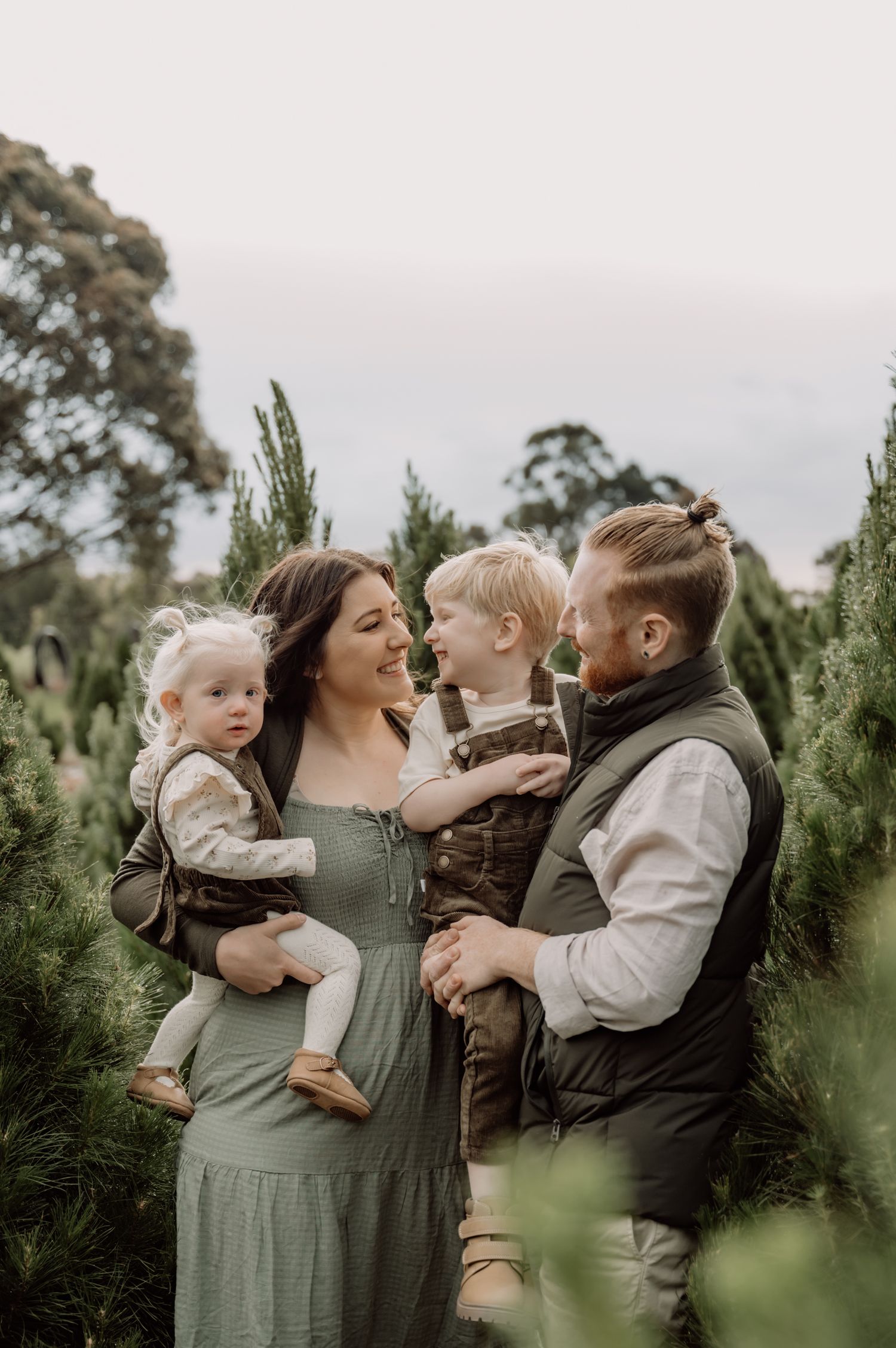 A family shares tender moments together among evergreen trees at an outdoor photo session.