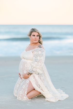 pregnant mama kneeling on the beach hugging her belly