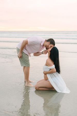 dad leaning over tp kiss pregnant wife at Jacksonville beach sunrise
