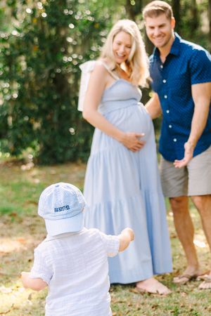 brother running up to pregnant mama and dad with hat that says big brother