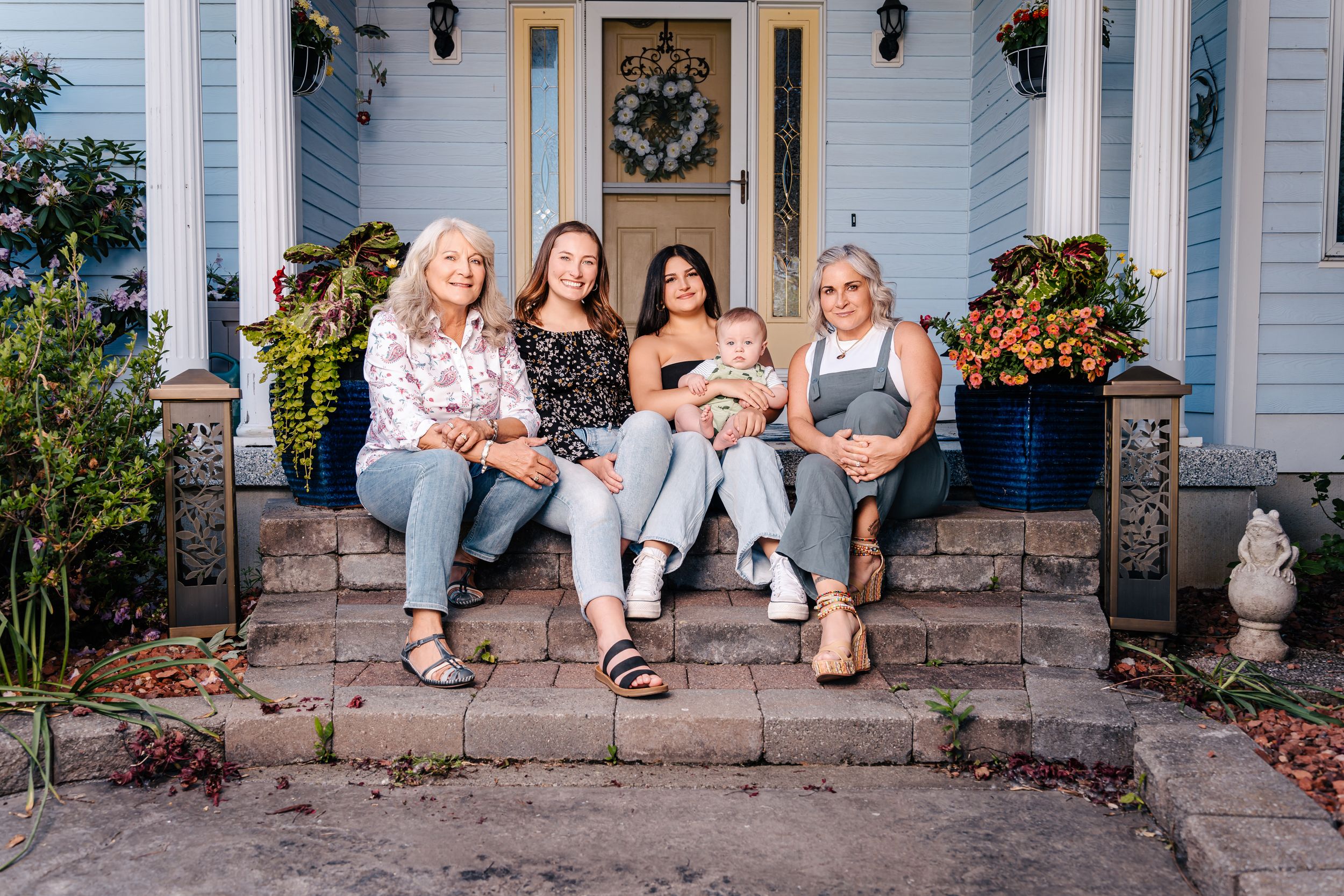 A group relaxes on front porch steps of a blue house with fall decorations.