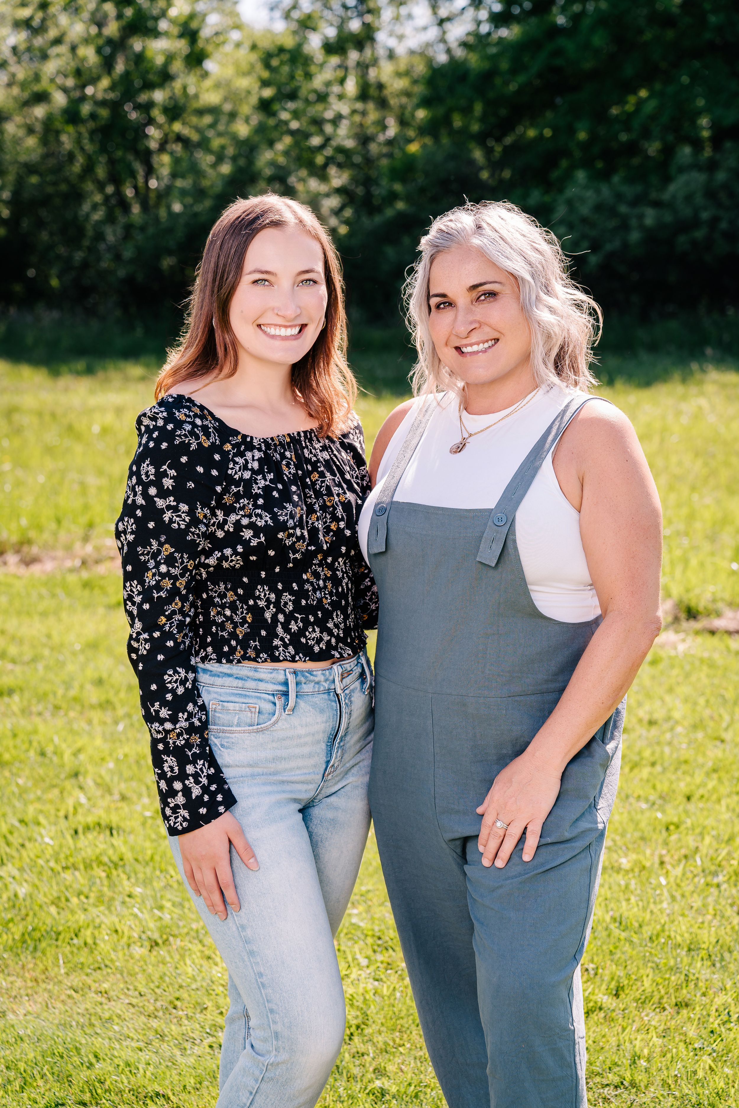 Two friends pose together on a sunny day in a grassy field.