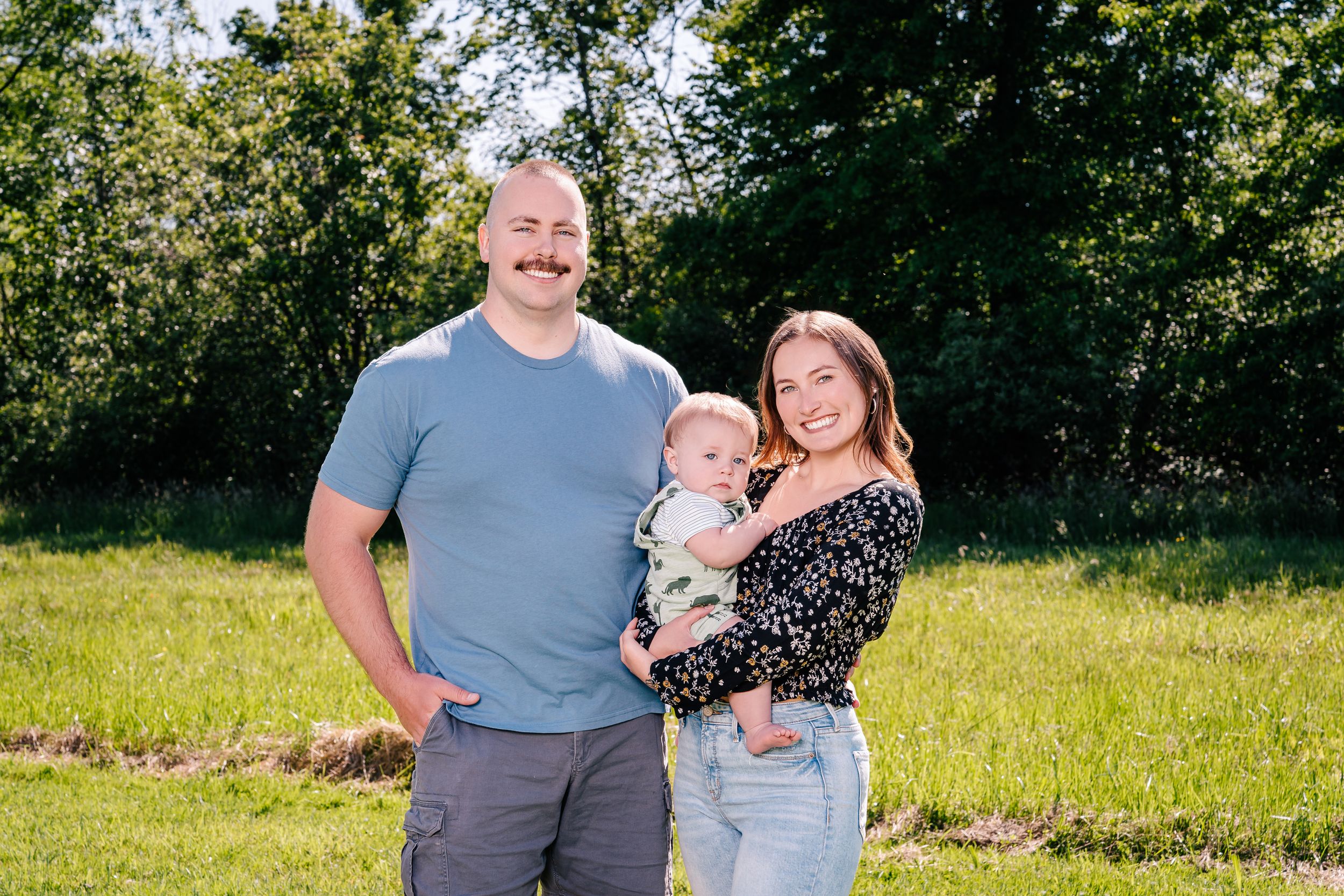 A family poses together on a sunny summer day in a grassy field.