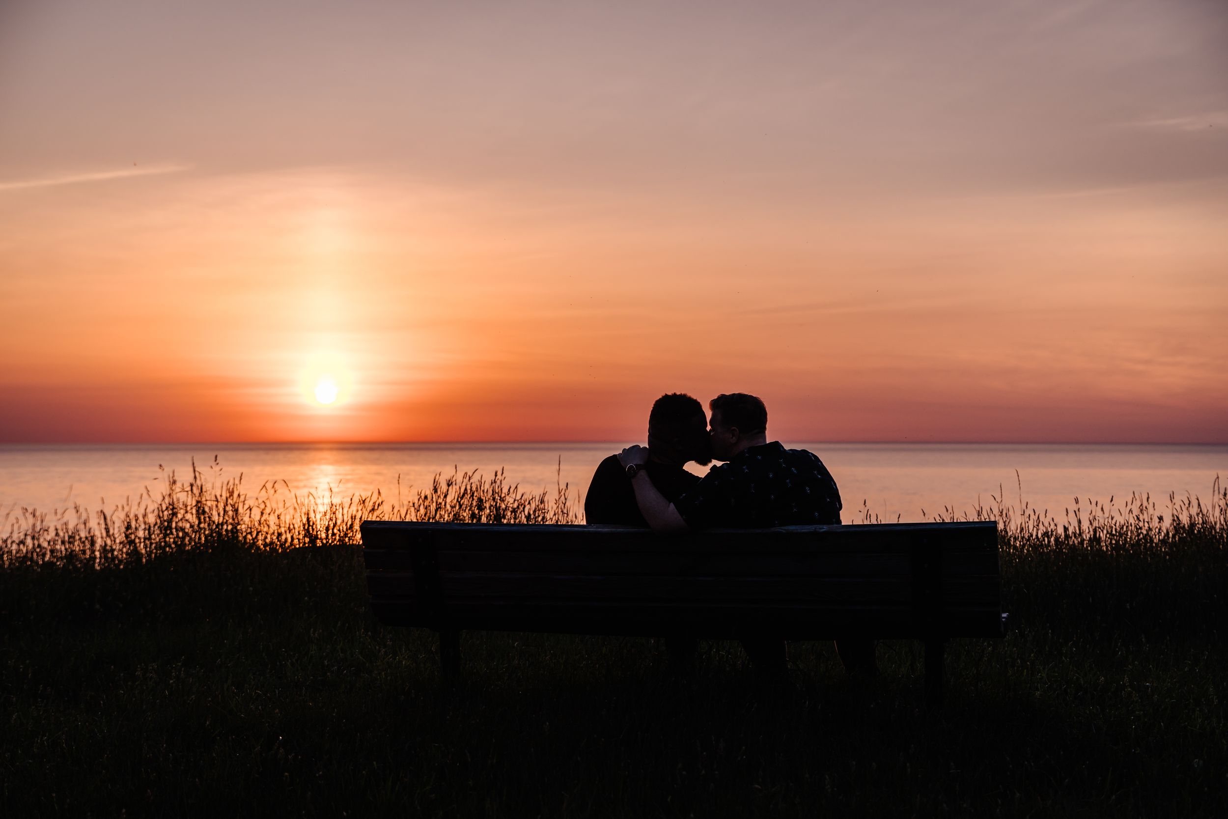 Silhouettes of a couple sharing an intimate moment on a bench during a spectacular ocean sunset.