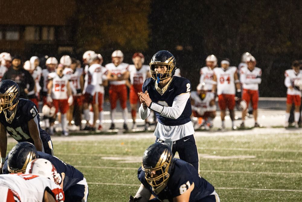 Football players in navy and red uniforms competing on the field at night at George Fox University.
