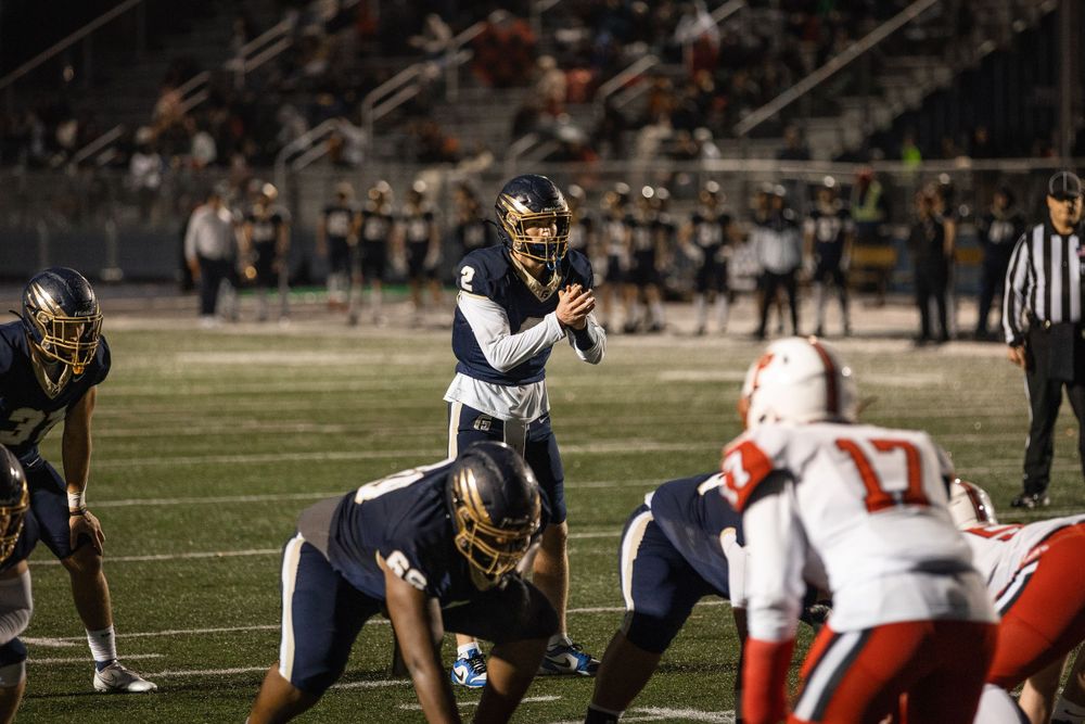 A quarterback in position behind the offensive line during a night football game at George Fox University.