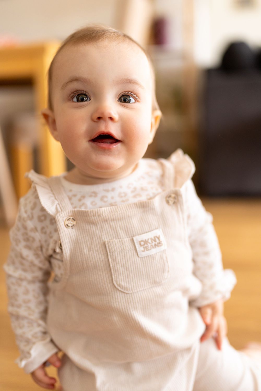A 1 year old baby in white clothing curiously smiling to the camera at home, Cambridge, UK