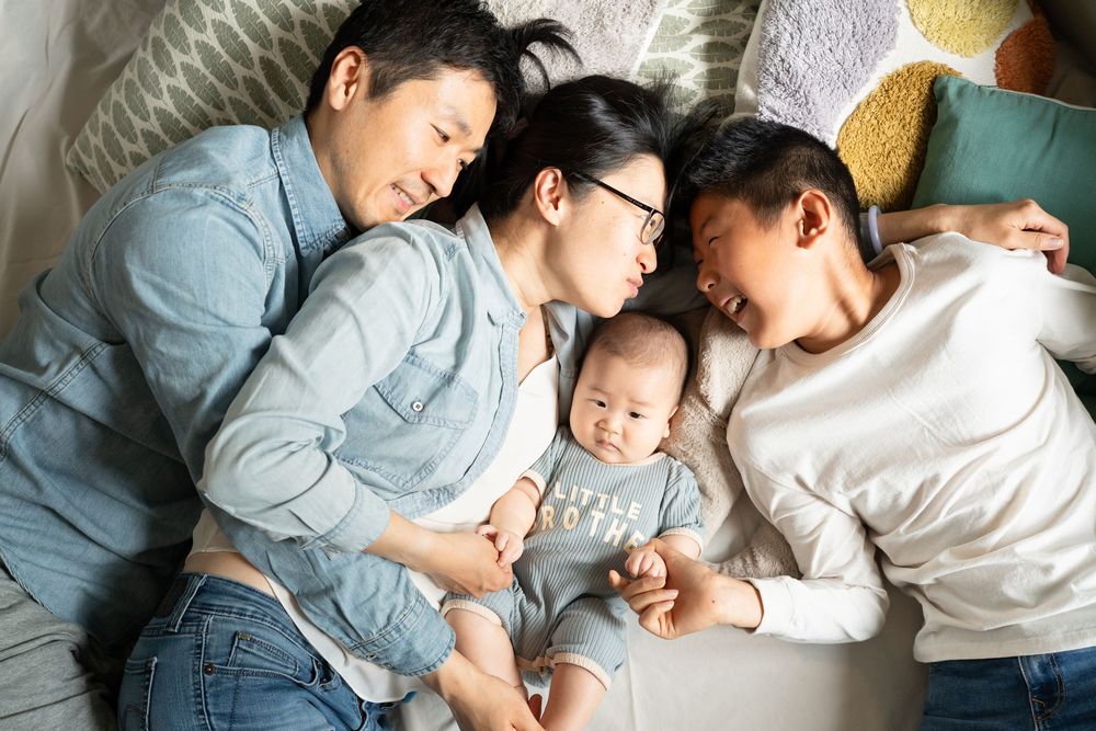 Parents and children napping together in comfy positions on clean white bedding on a bed. Cambridge, UK