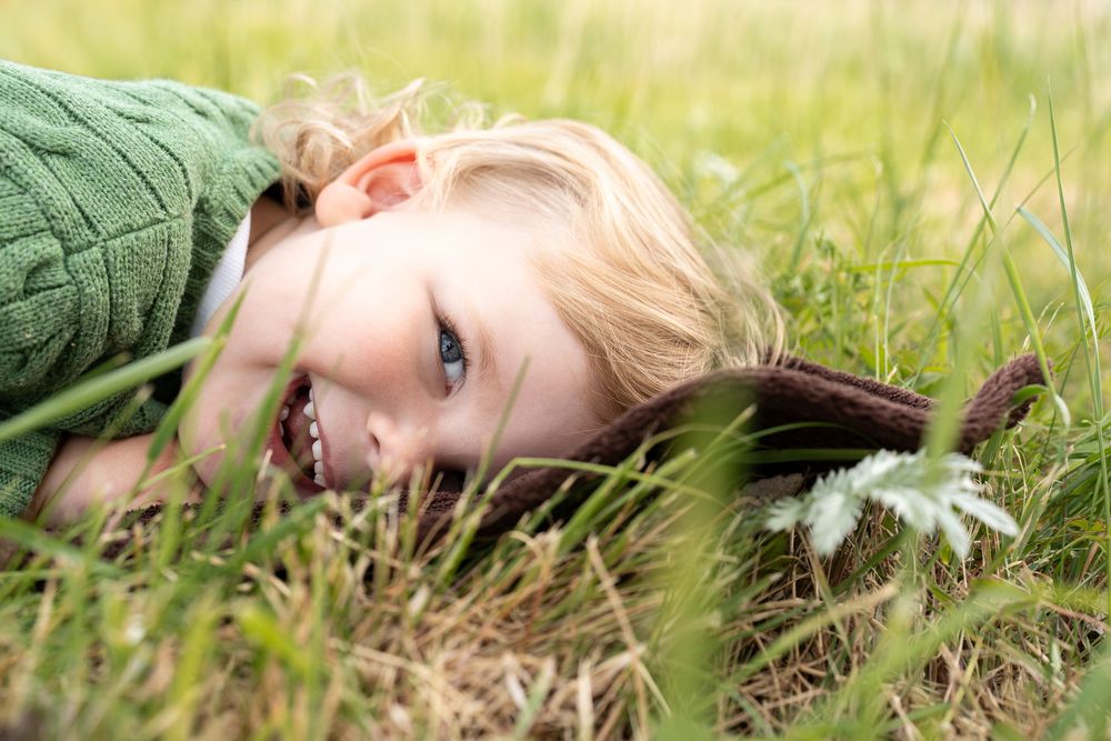 A joyful toddler lying in tall green grass during a bright sunny day in Cambridge, UK