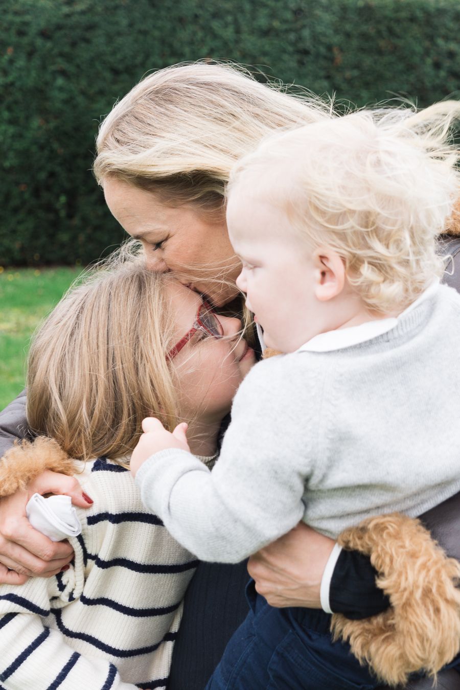 A mother kissing her daughter while holding a baby at their house in Cambridge, UK
