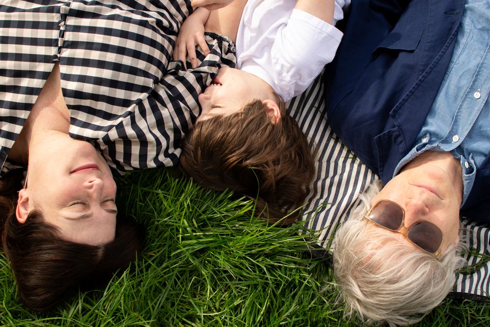 Family laying on grass during their outdoor activity in Granchester Meadows, Cambridge, UK