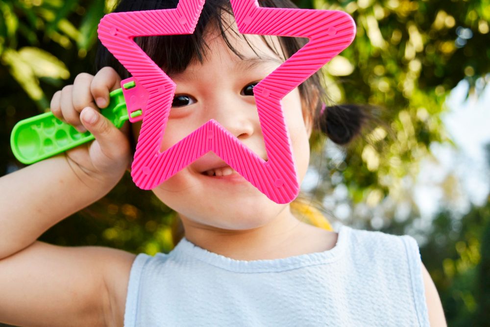 A smiley child with a pink toy in the park, Granchester Meadows, UK