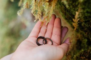wedding rings in hands with a water drop falling on them from moss. Photo by Washington Elopement Photographer, Pine + Vow.