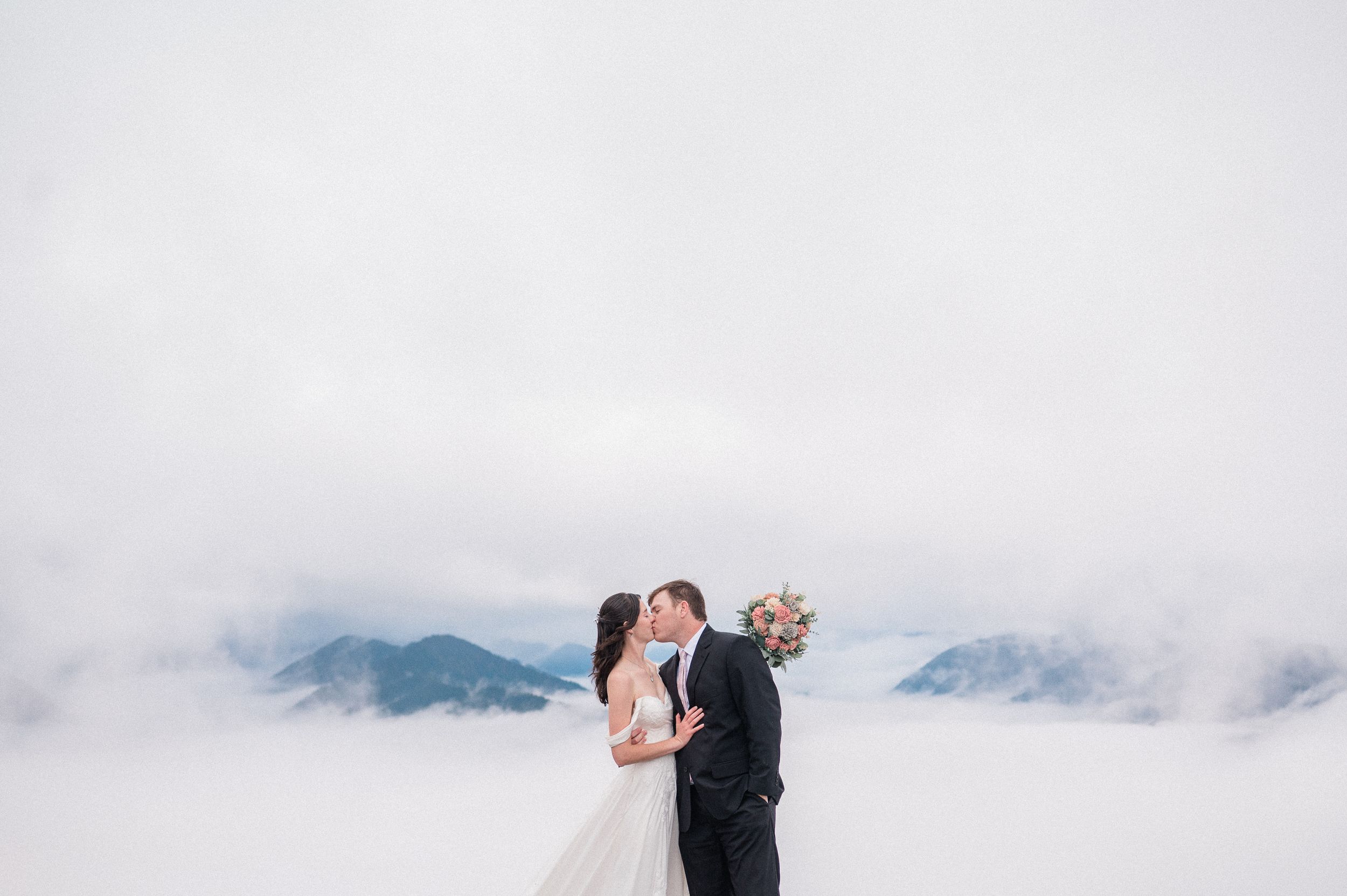 bride and groom kissing with blue mountains and clouds behind them