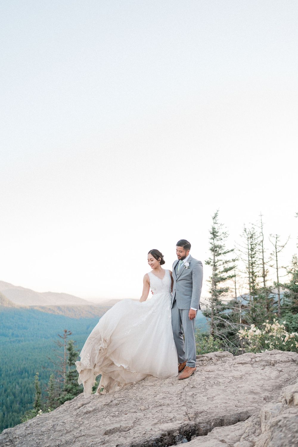 A bride and groom stand together on a mountain cliff overlooking a forested valley during a scenic outdoor Washington elopement.