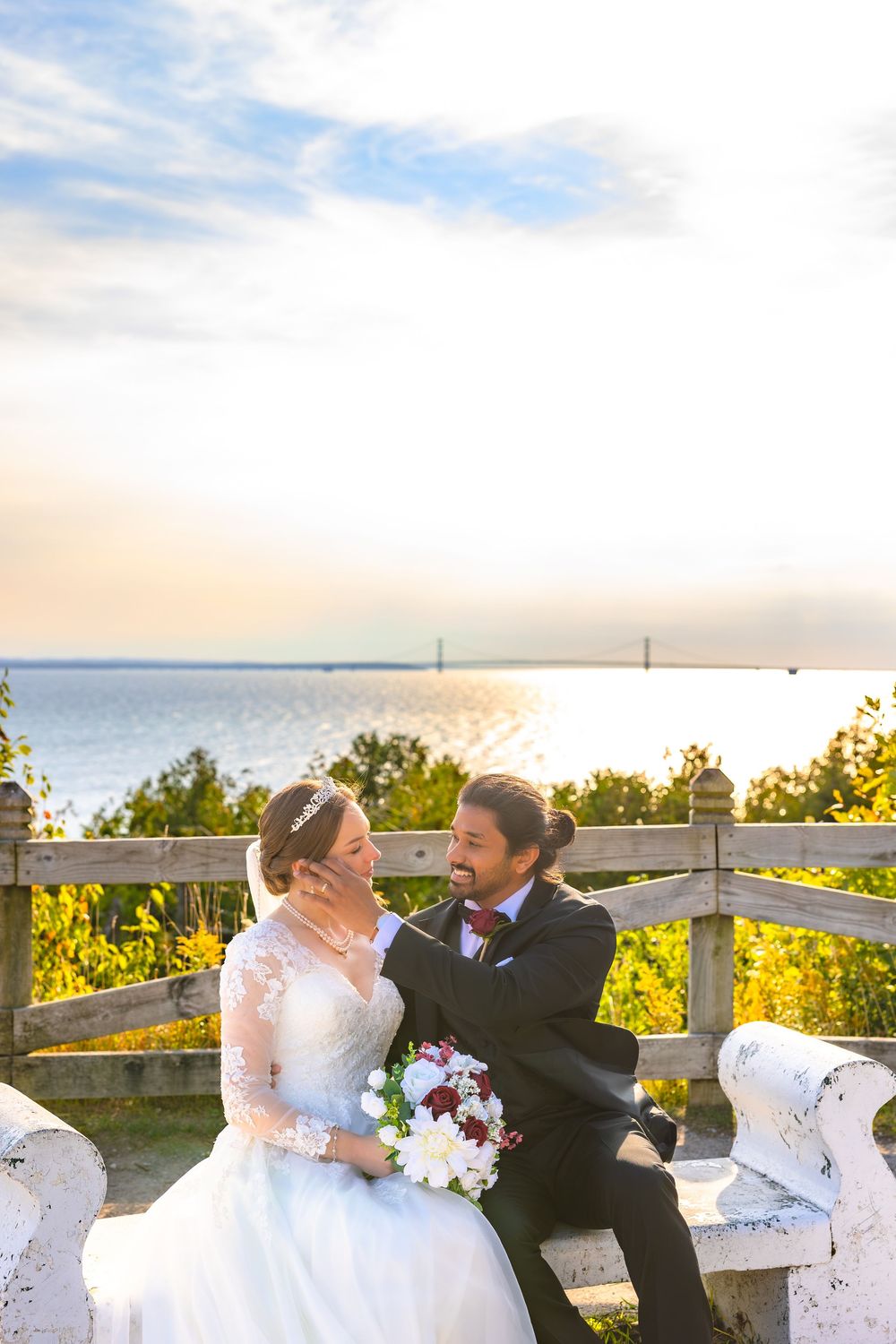 A couple shares a romantic moment on a scenic overlook with ocean and sunset views in the background.