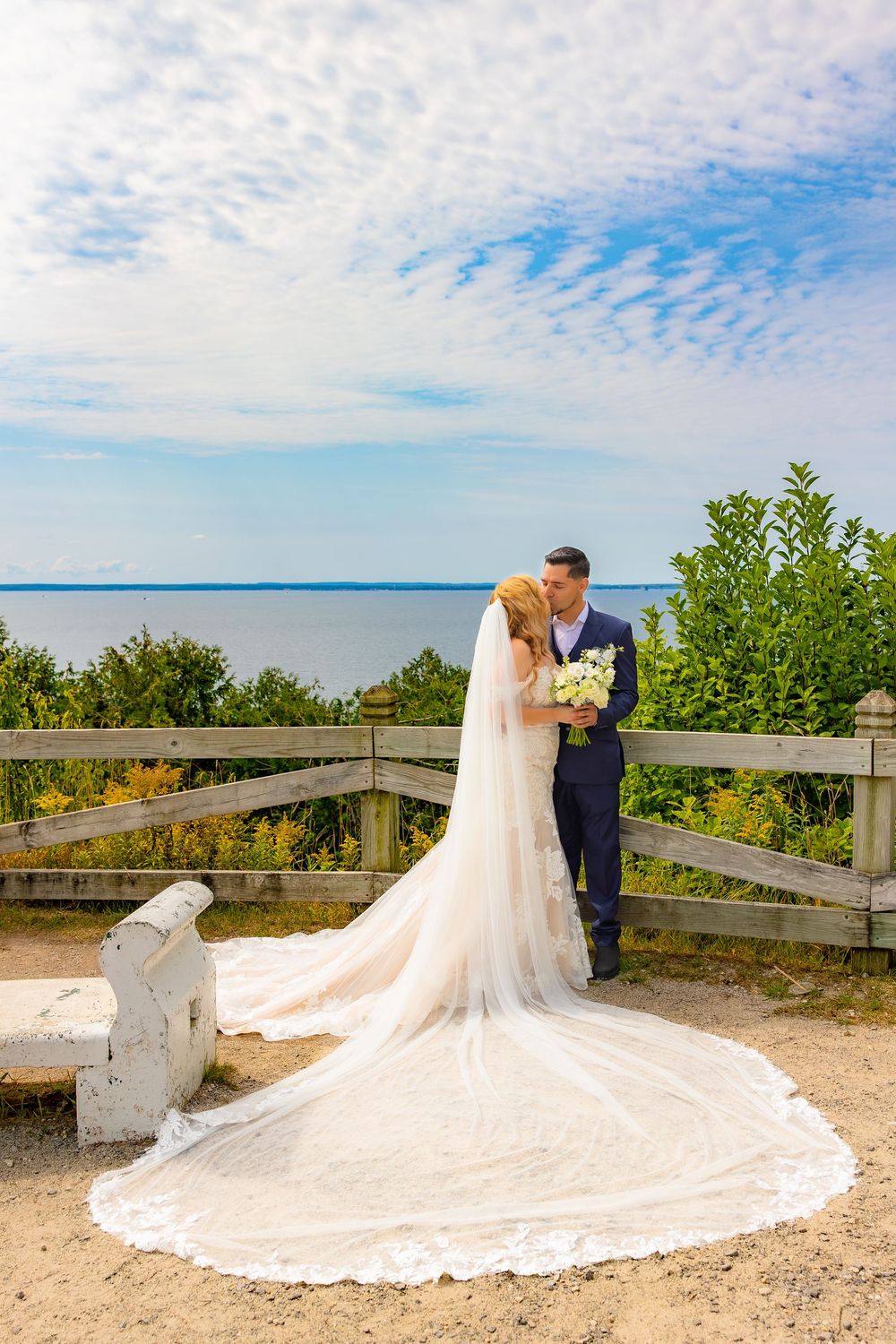 A romantic beach wedding photoshoot featuring a long cathedral veil trailing in the sand at sunset.