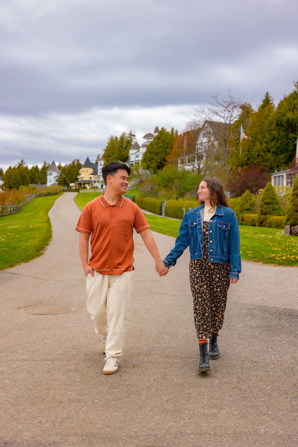 A couple walks hand in hand along a winding path through a scenic hillside park on an overcast autumn day.