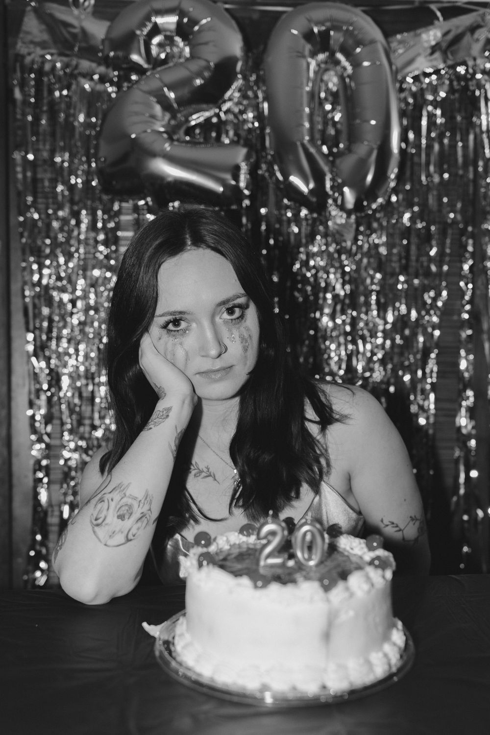 A person sits at a table with a 20th birthday cake and silver decorations in the background.